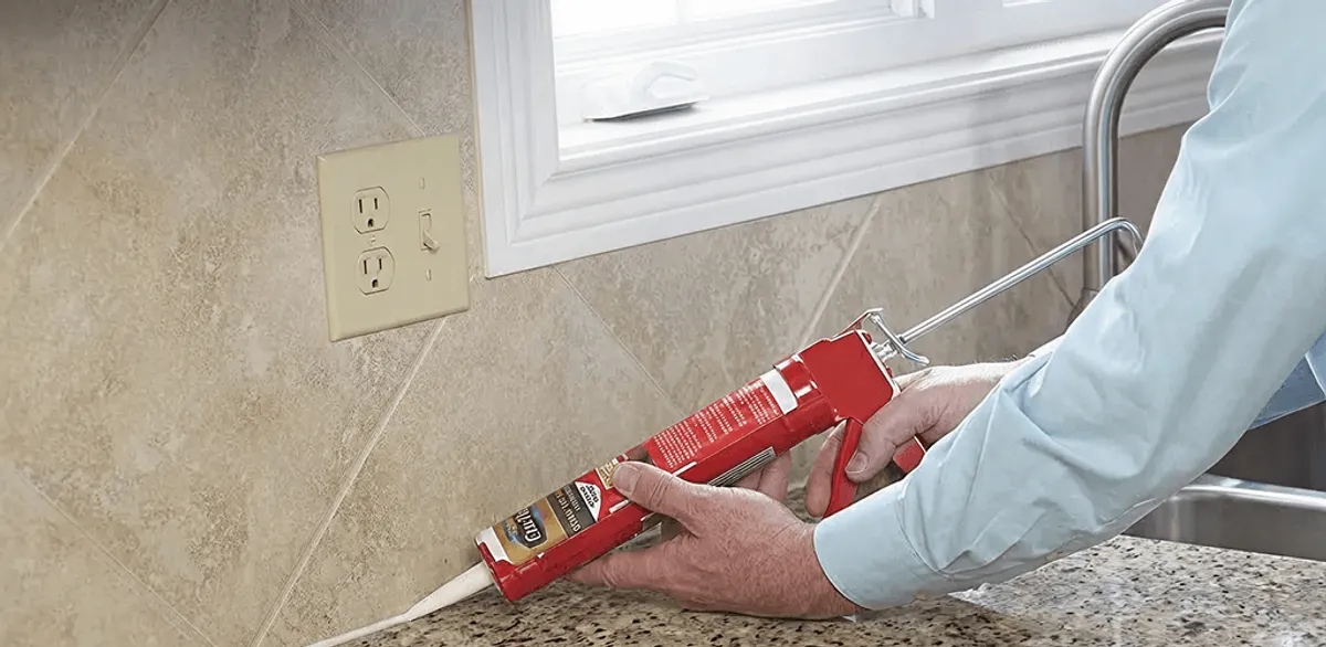 Handyman applying caulk along a kitchen backsplash and countertop seam in Long Beach, CA