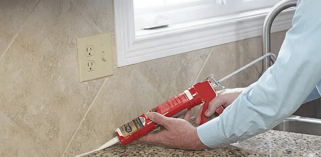 Handyman applying caulk along a kitchen backsplash and countertop seam in Long Beach, CA